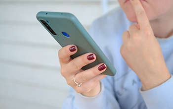 Eine Person hält ein Smartphone in der Hand und legt sich nachdenklich den linken Zeigefinger auf die Lippen
